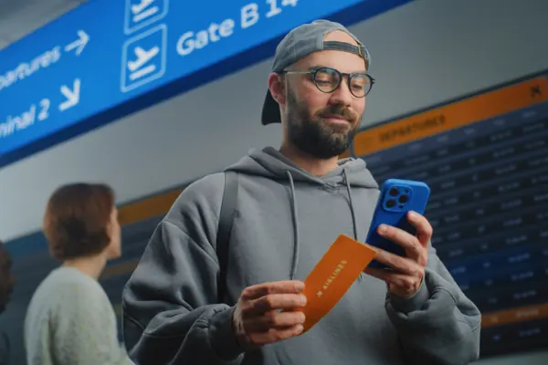 Viajero consultando su móvil frente al panel de salidas del aeropuerto